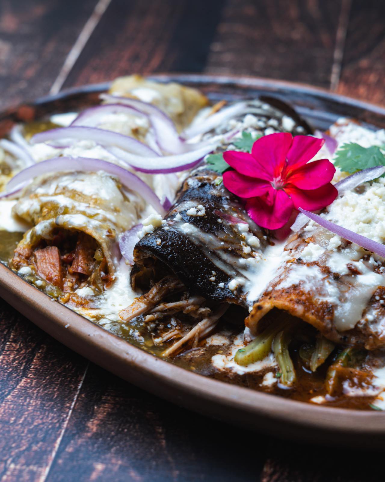 Enchiladas verdes con crema, cebolla morada y flor comestible.